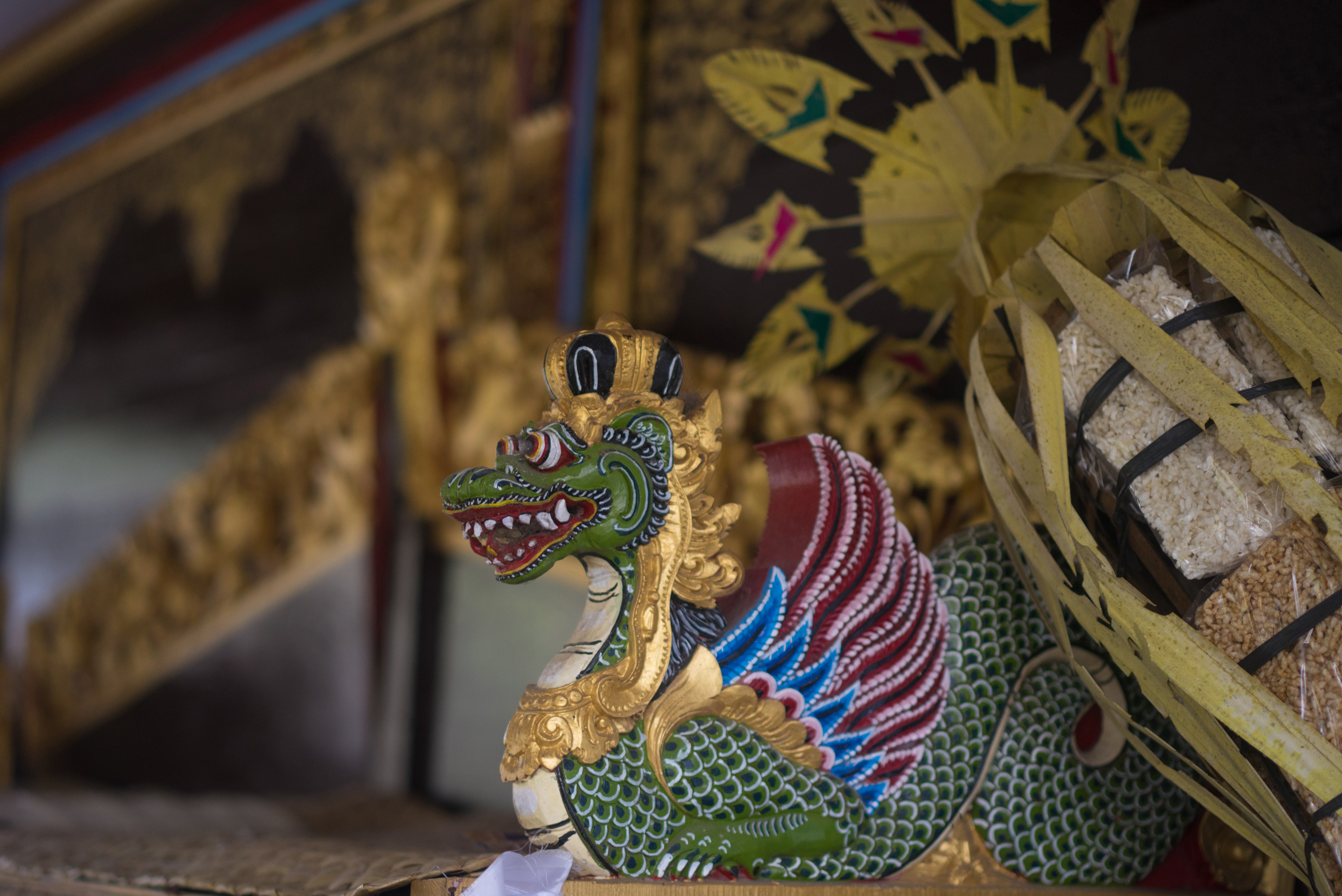 A Naga sits with a crown atop its head and rice offerings can be seen